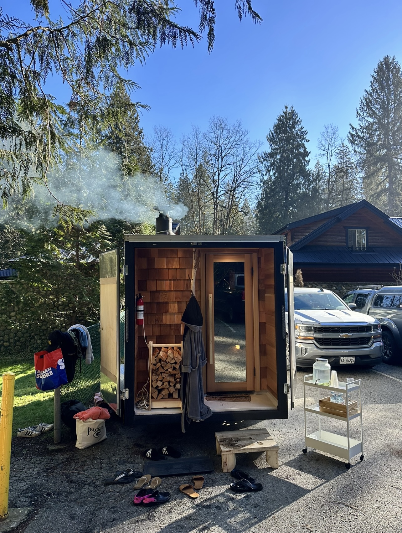 The custom wood sauna set up outdoors with steam rising from its chimney